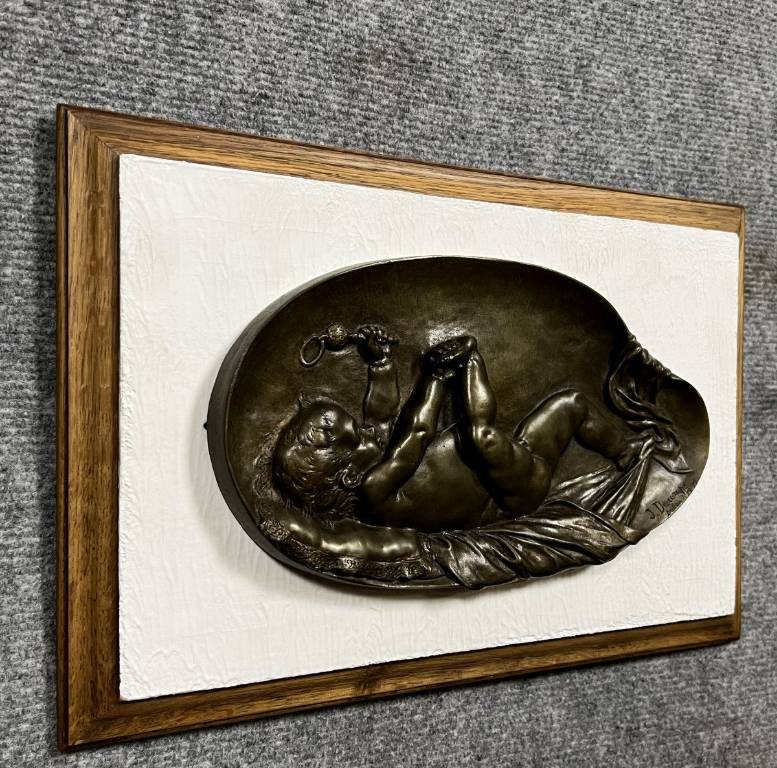 bas relief en bronze figurant un bébé jouant avec son pied et tenant un hochet dans l'autre main. | Puces Privées